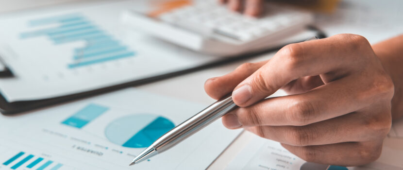 Table filled with paper with graphs and pie charts on as someone uses a calculator