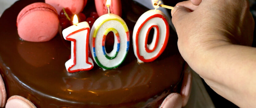 Someone lighting candles on a 100th birthday cake.